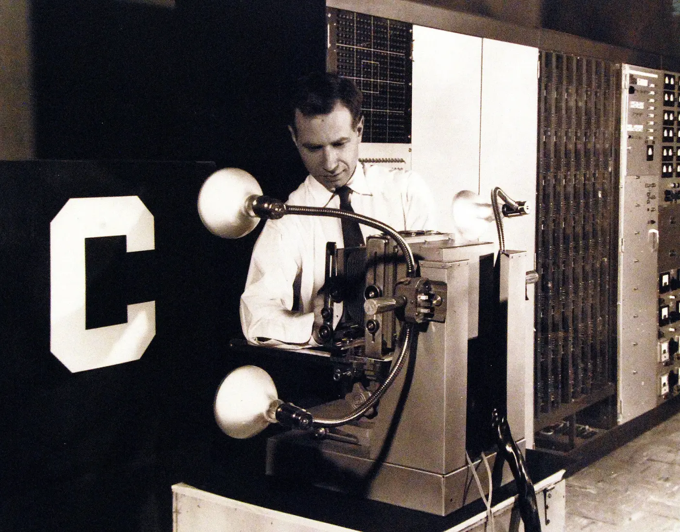 A man in shirt and tie adjusts the camera of the Mark I Perceptron, which points at a large letter C