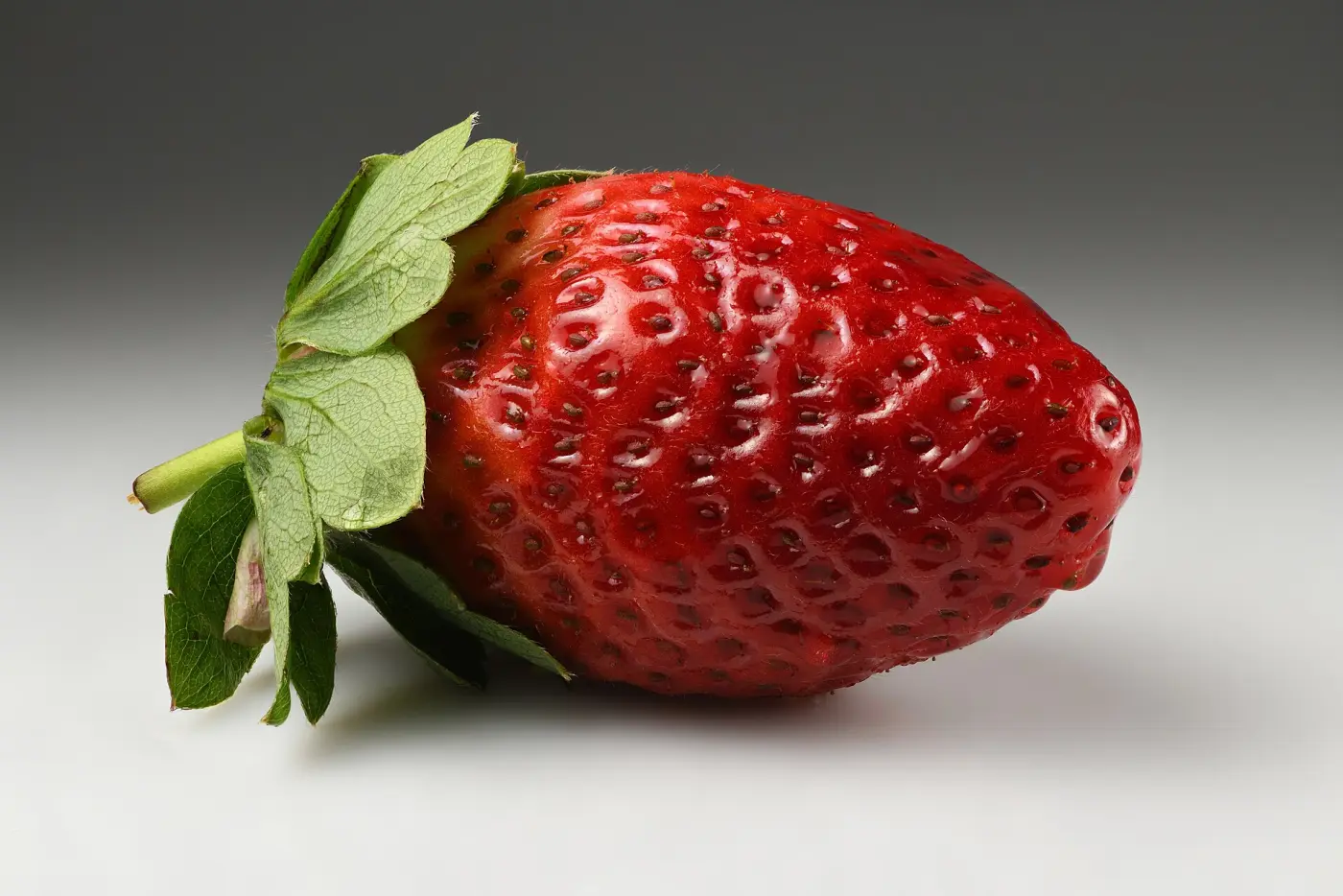 A single red strawberry with its green calyx against a light background