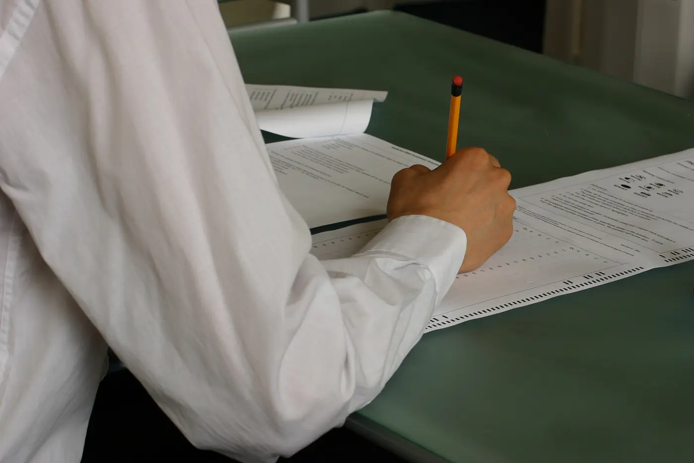A hand filling in an exam paper with a pencil