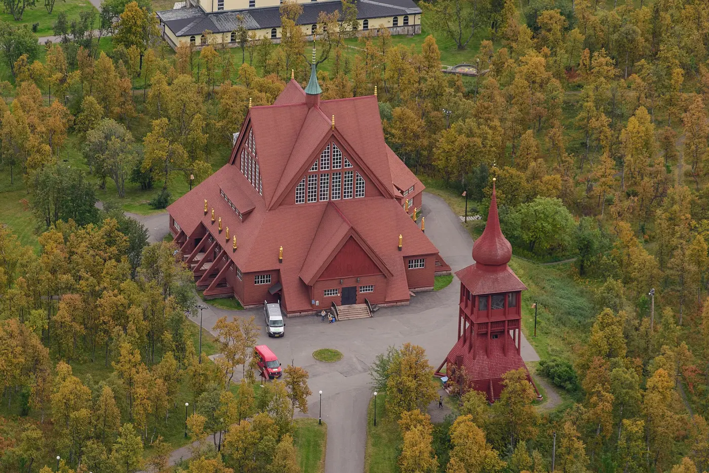 Aerial view of a large red wooden church with a separate bell tower among autumn-yellow birches