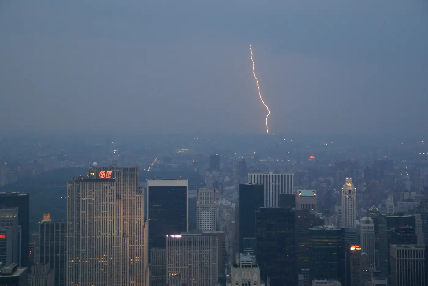 View from the Empire State Building over Manhattan at dusk, lightning strikes in the distance
