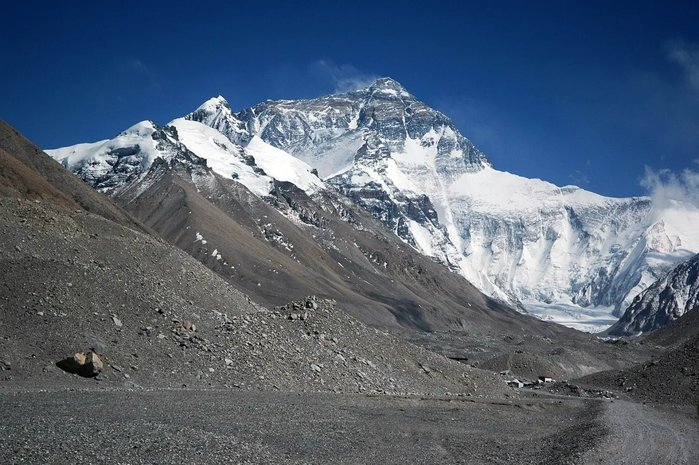 Mount Everest with its snow-covered north face at the end of a stony valley under a blue sky