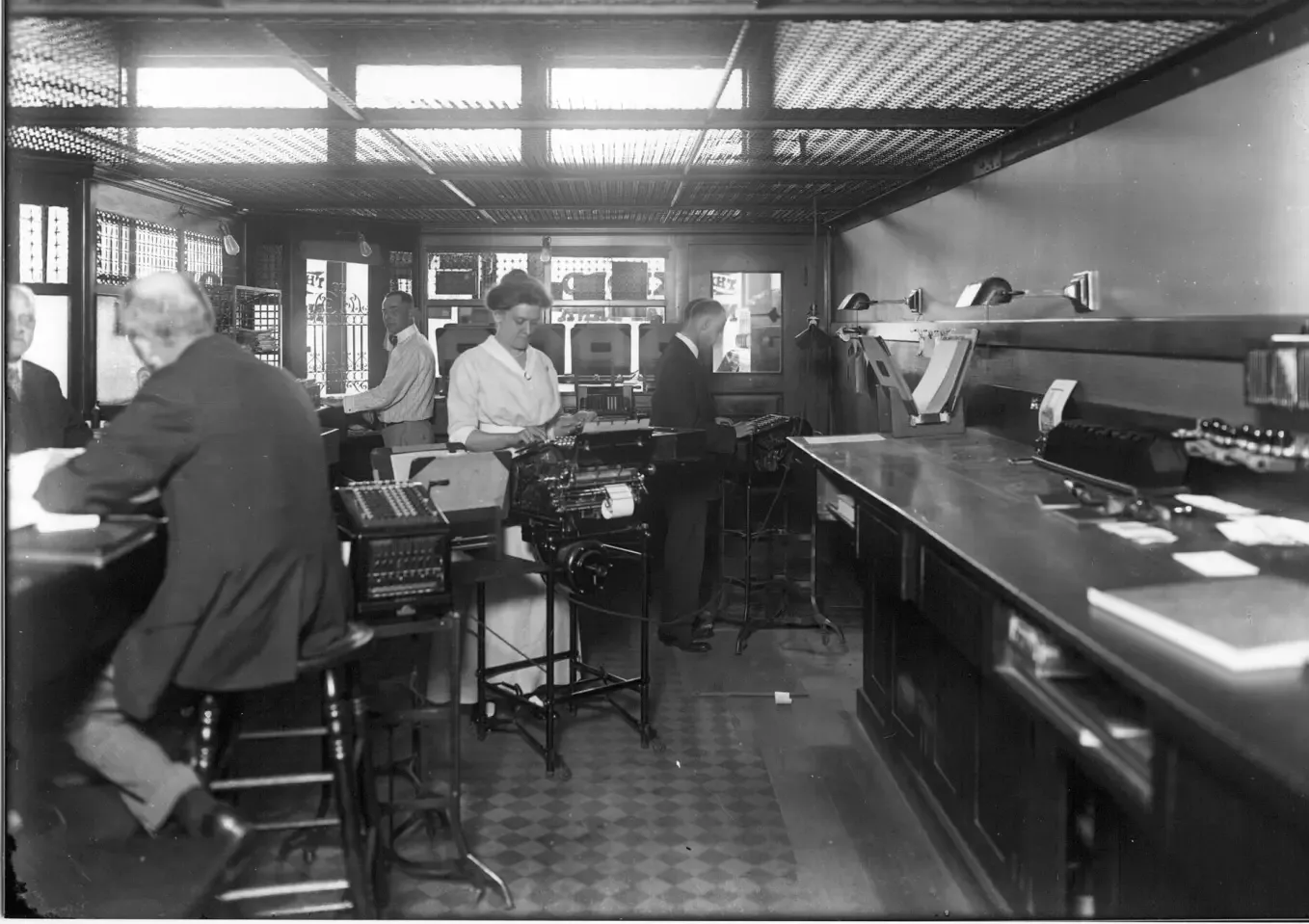 Black-and-white photo: clerks behind the counter of a bank, 1916